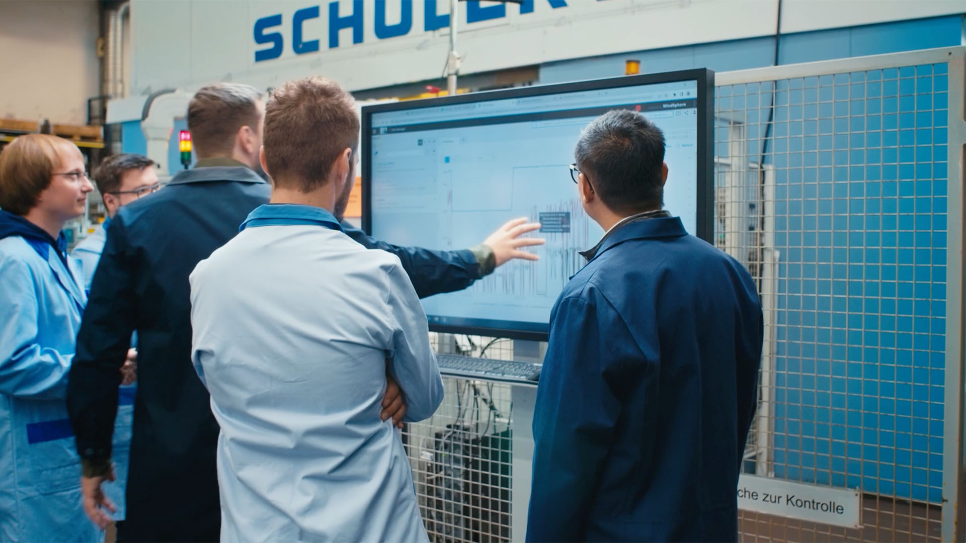 Mitarbeitende in Arbeitskleidung stehen vor einem großen Bildschirm mit technischen Daten und Diagrammen.