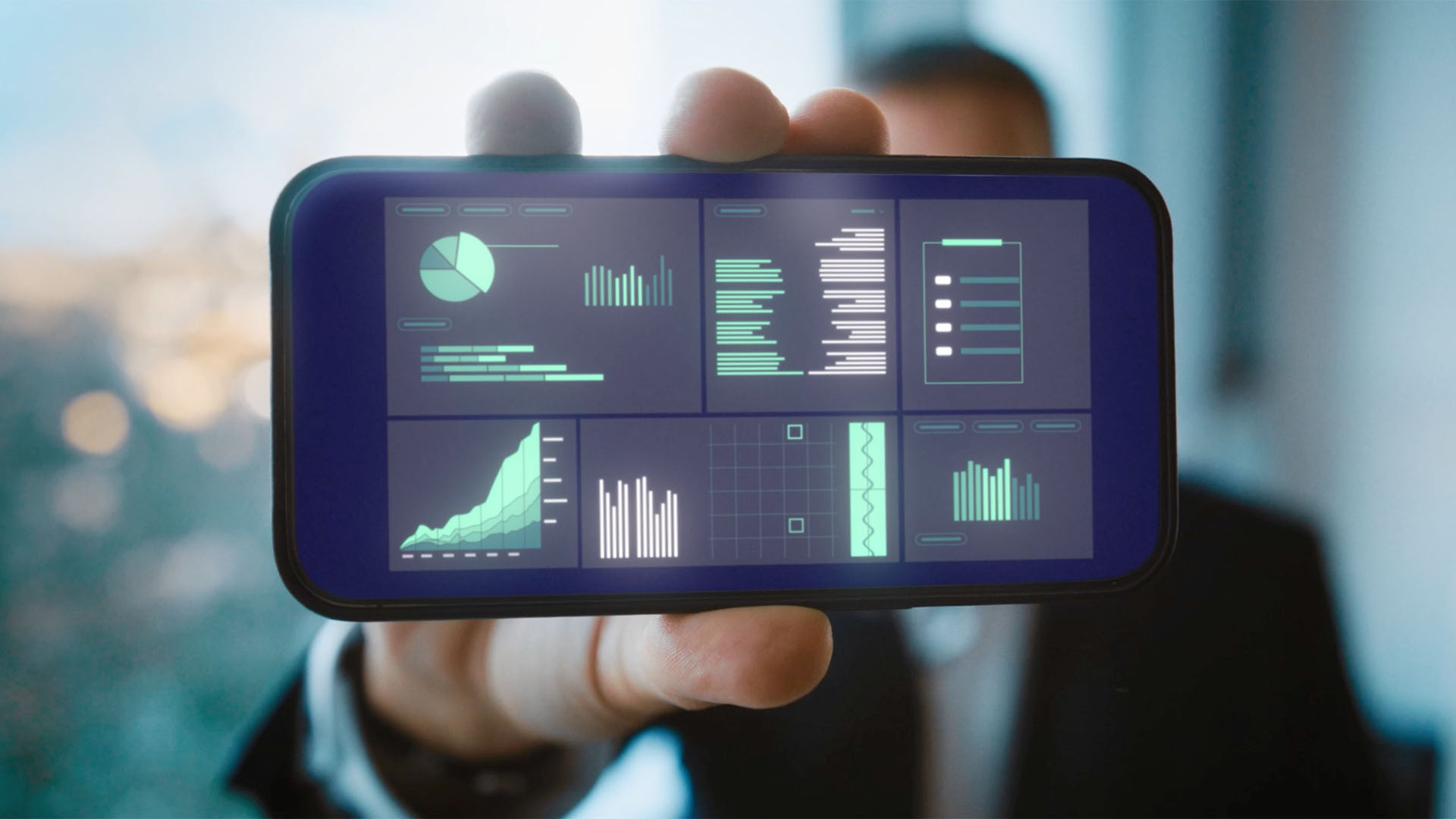 Hand hält ein Smartphone, das mehrere Analyse-Charts und KPIs zeigt