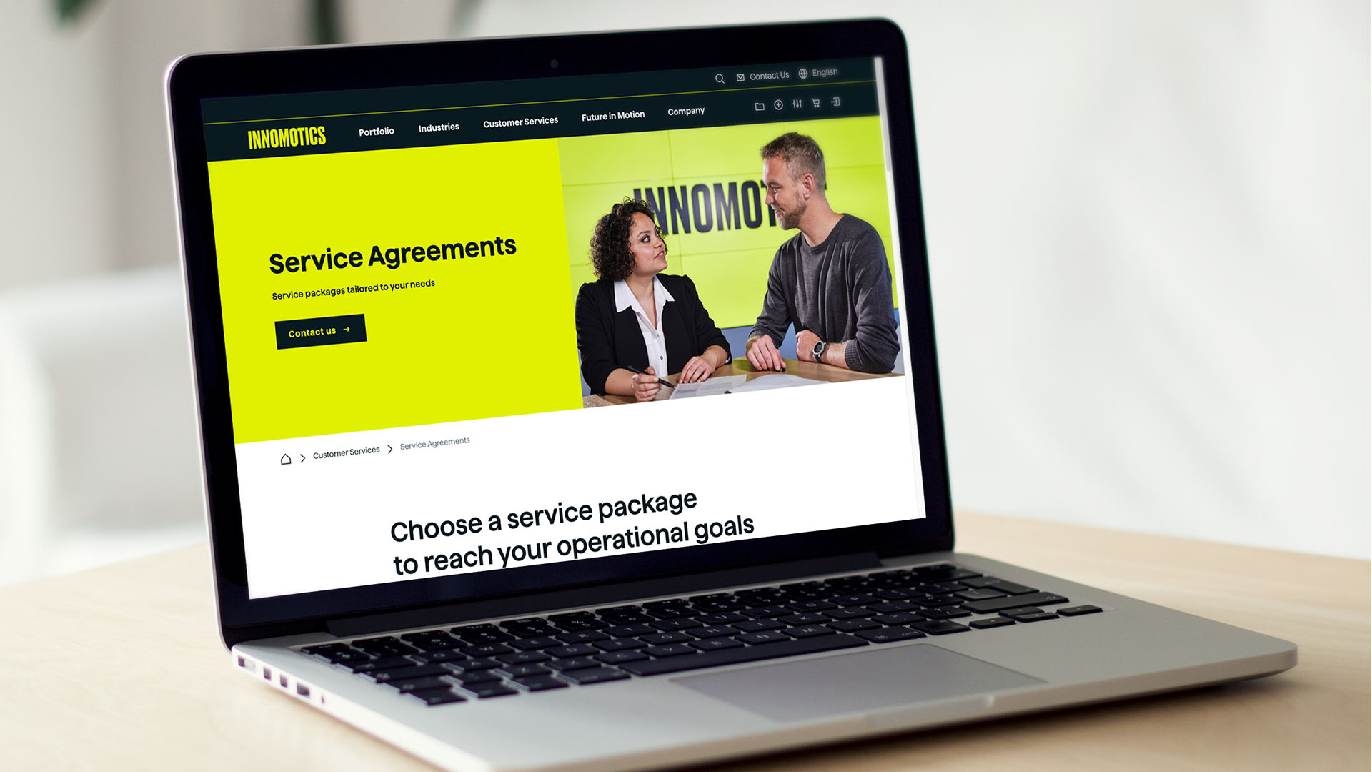 Laptop mit der Innomotics-Webseite ‚Service Agreements‘ und Foto zweier Personen im Gespräch.