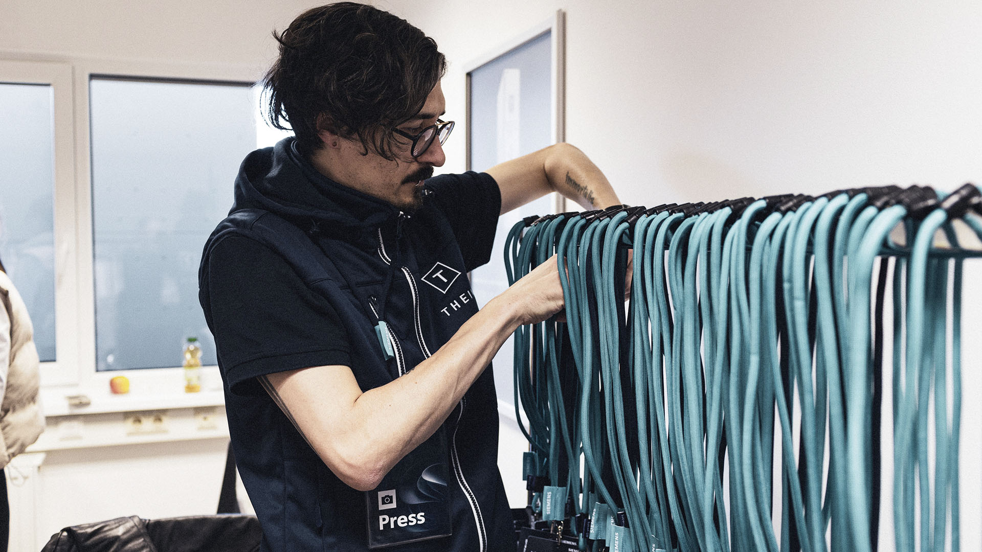 Ein Mitarbeiter von Theim Kommunikation sortiert zahlreiche türkisfarbene Lanyards an einem Kleiderständer.