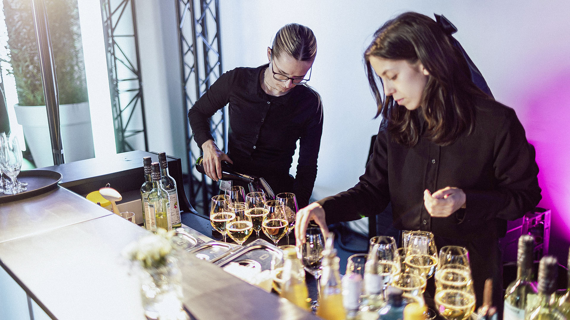 Zwei Servicekräfte schenken an einer Bar Weißwein und Getränke bei einem Event ein.