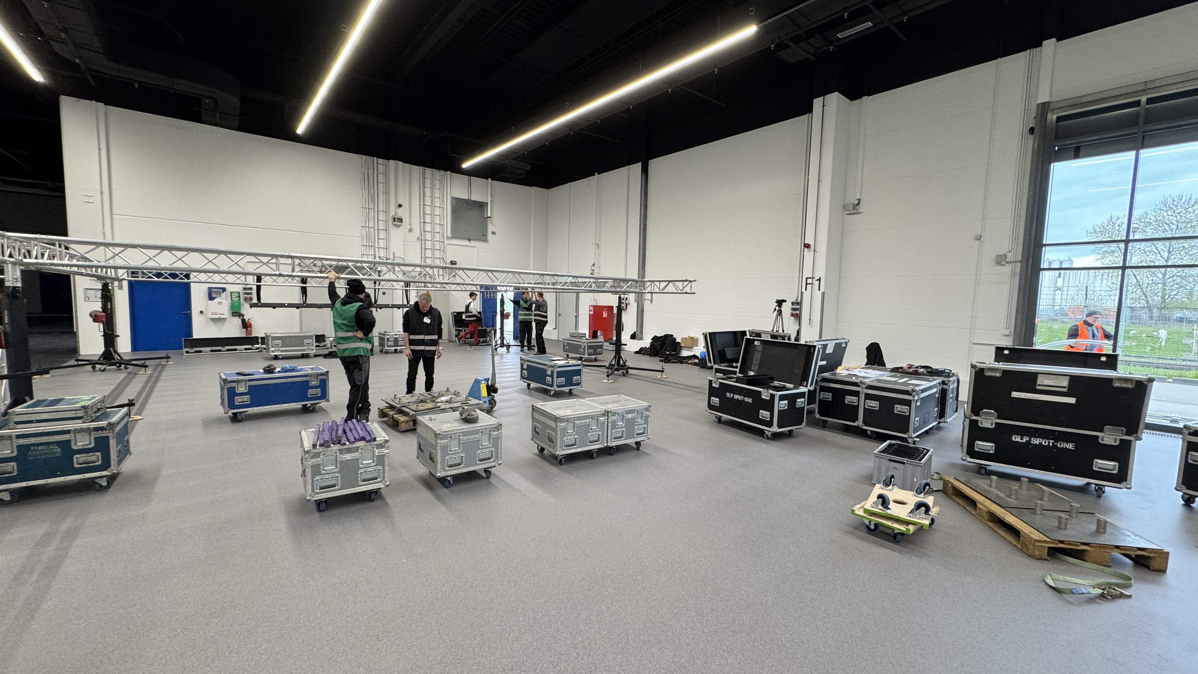 Veranstaltungstechniker richten in einer leeren Halle Traversen ein und stehen zwischen vielen Transportkisten und Equipment.