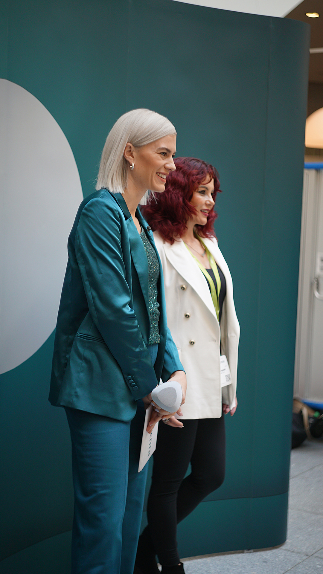 Zwei Frauen posieren im Messeumfeld vor einer grünen Markenfläche.