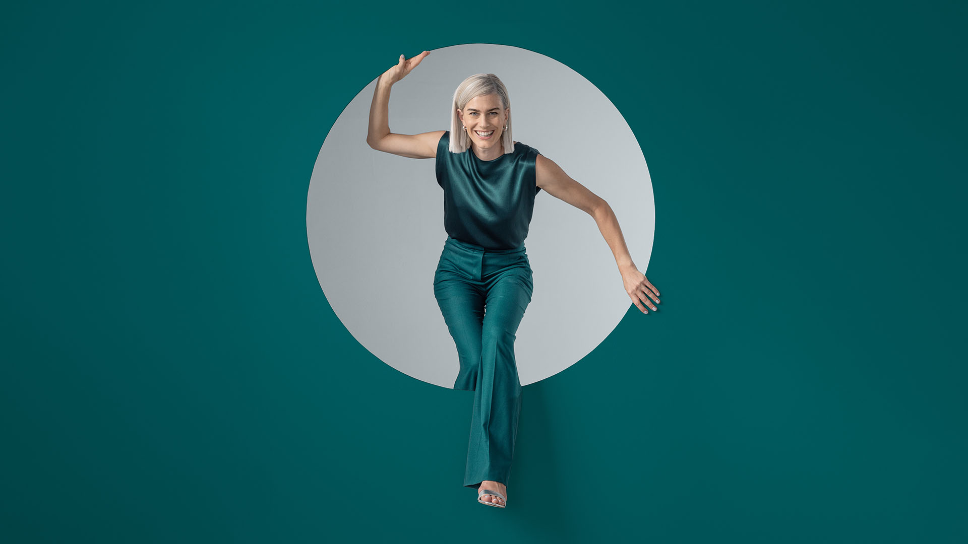 Frau in smaragdgrünem Outfit, die dynamisch durch einen kreisförmigen Ausschnitt tritt.